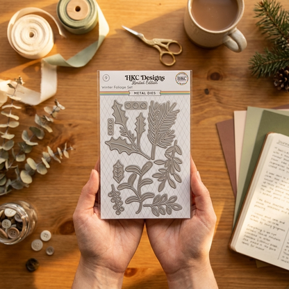 HKC Designs metal dies with floral patterns held by hands on a wooden table with crafting supplies.